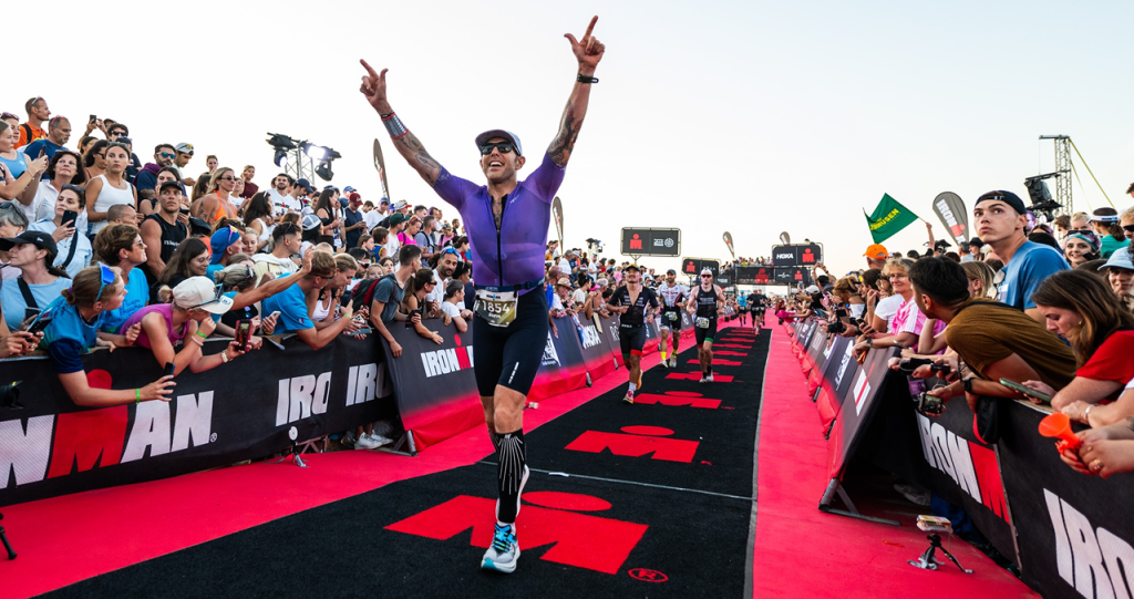 Steve crosses the finish line in a purple race suit arms aloft